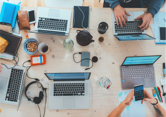 Top down view of people working on laptops at a large desk