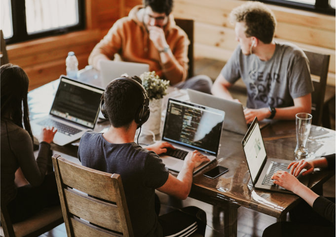 A group of people working at a desk on laptops